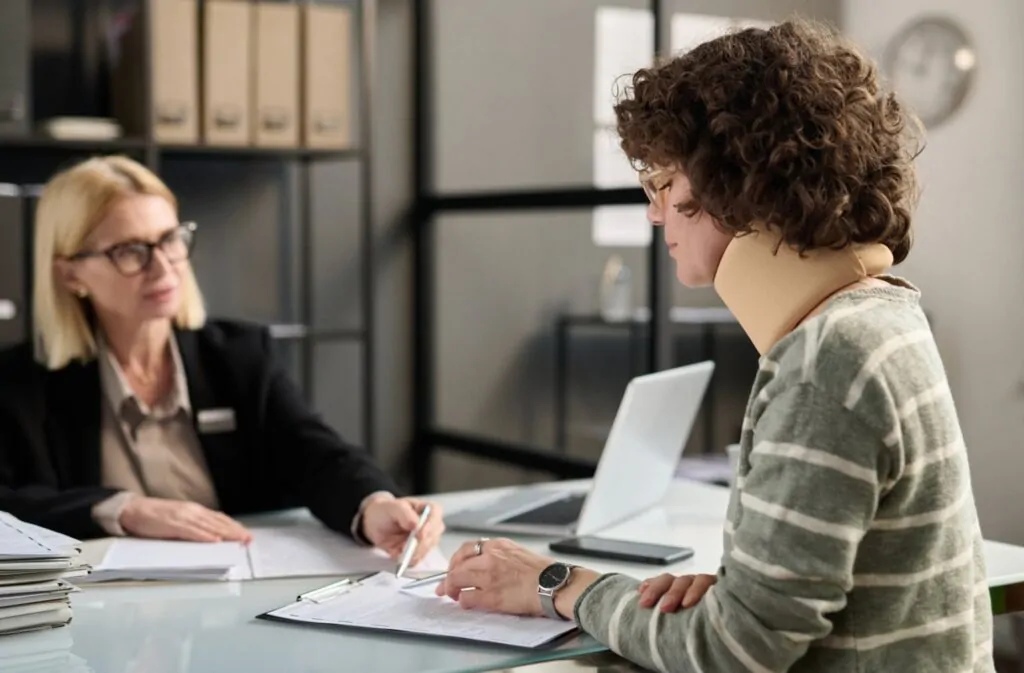 What happens without health Insurance: young woman with neck injury filling out insurance documents at an office
